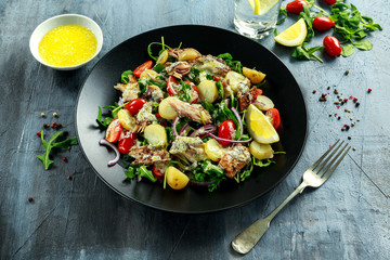 Smoked Mackerel Salad with warm boiled new potato, cherry tomatoes, chopped red onion and Ruccola on black plate.