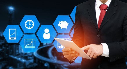 smart businessman in suit using his tablet with financial icon business and technology concept on blurred night city background, color tone effect.