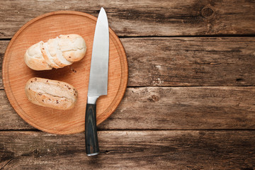 Fresh baked bread buns on platter with knife, on wooden table, flat lay. Food background with free space for text. Bakery, homemade pastry, cooking concept