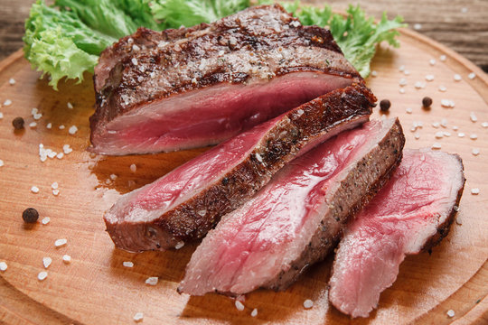 Thick slices of superior grilled beef steak decorated with lettuce leaf, served on wooden table, close up view. American food. Menu photo.