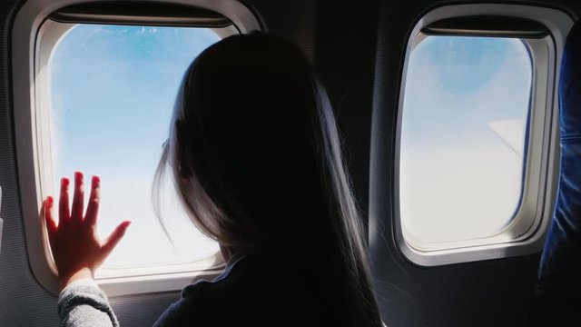 The girl is 6 years looking at the airliner window. The view from behind, in the frame are visible portholes
