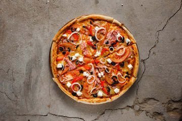 Delicious colorful hot italian pizza with ham, tomatoes, olives, onion and feta cheese on concrete background with copy space, flat lay.