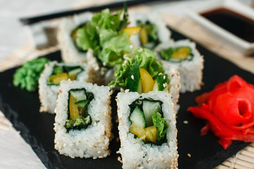 Appetizing and yummy sushi uramaki rolls with avocado, cucumber and lettuce, served on black slate with ginger and wasabi. Japanese delicacy for gourmet.