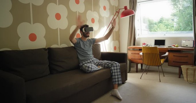 Young man wearing virtual reality headset having video chat sitting on sofa at home watching 360 video imagination concept retro styled modern apartment