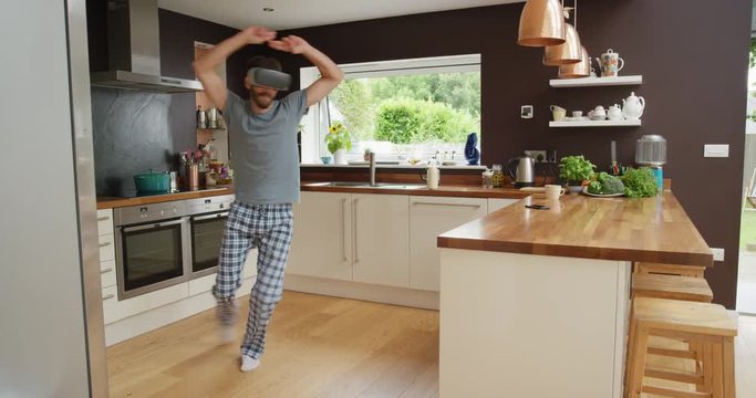 Happy young man wearing virtual reality headset dancing in kitchen wearing pajamas in the morning listening to music 360 video imagination concept