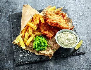 British Traditional Fish and chips with mashed peas, tartar sauce on crumpled paper.
