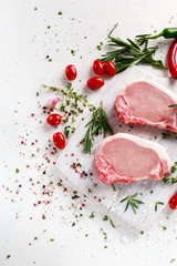 Raw Pork Loin chops on a cutting board with herbs, rosemary, thyme, chilli, salt, pepper on white cutting board.