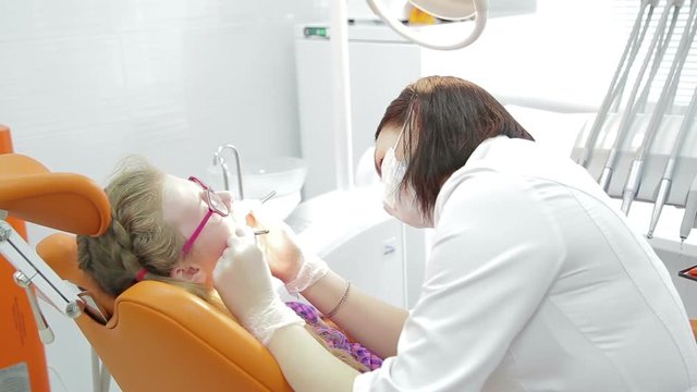 Closeup of dentist examining young woman's teeth. Dental care concept. Close up of a open mouth while the dentist sisiting the patient. Oral hygiene at dentist office. Close up of a white teeth.
