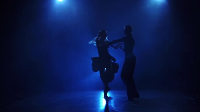 Silhouette of pair dancers performing latin dance in slow motion
