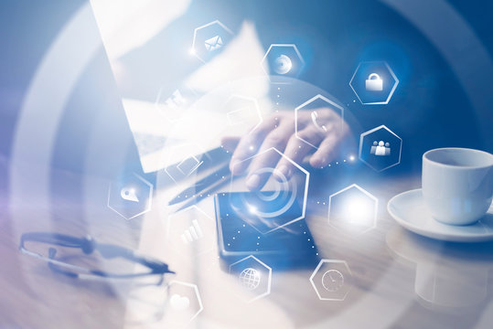 Concept of virtual screen,connections icon and digital interfaces.Businessman working at office on laptop.Man pointing hand on thouch screen of smartphone.Blurred background.