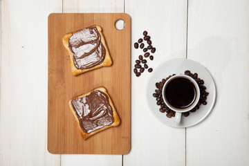 cup of coffee and toast with chocolate on a white wooden table