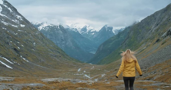 Woman with arms raised looking at mountain view in glacial valley wearing yellow Jacket Girl lifting arm up celebrating scenic landscape enjoying vacation travel adventure nature Norway