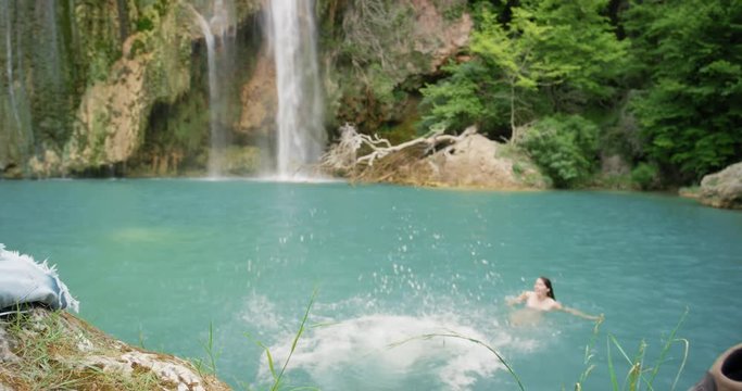 Young woman jumping into water wild swimming in natural pond at base of hidden waterfall Best friends girls in nature enjoying carefree vacation outdoors adventure