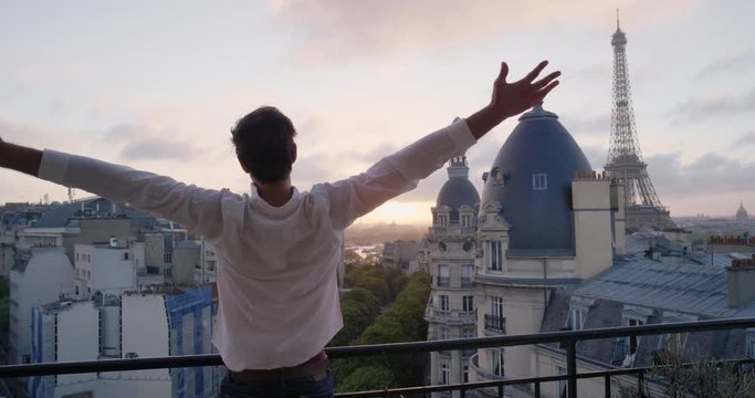 Young tourist man stretching in morning on hotel balcony with view of Eiffel Tower Paris arms raised enjoying european travel adventure celebrating beautiful city sightseeing exploration