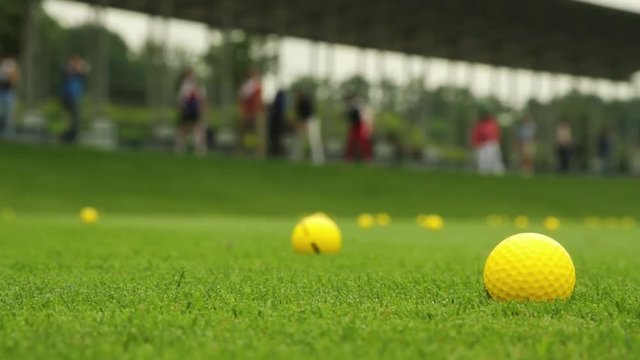 Yellow golf balls on the grass and driving range with people on training in the background 