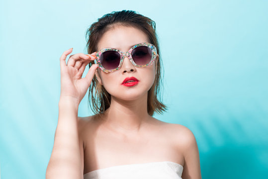 Colorful portrait of young attractive asian woman in sexy dress and wearing sunglasses over blue background. Summer beauty concept