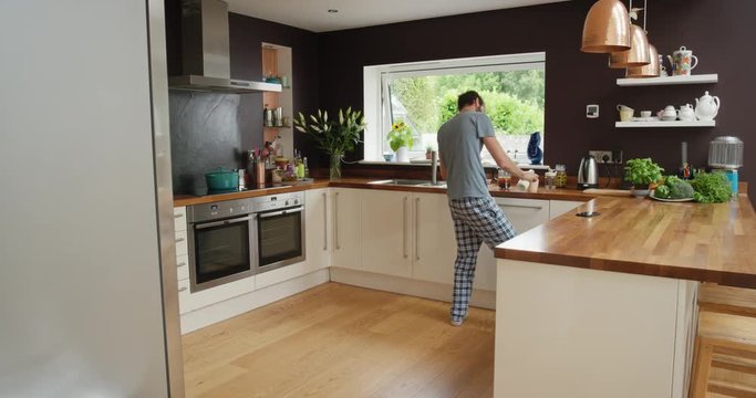 Man dancing in kitchen wearing pajamas in the morning listening to music on smartphone 