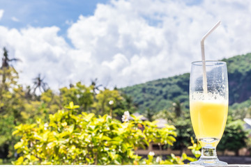Glass of orange juice on bright tropical blurred background with palms, outdoors. Tropical Bali island, Indonesia.