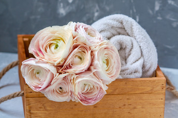 Ranunculus bouquet bath towel in wooden box. Spa concept and space for text.