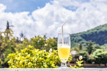 Glass of orange juice on bright tropical blurred background with palms, outdoors. Tropical Bali island, Indonesia.