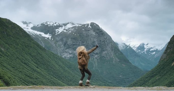 Woman dancing silly freestyle dance outdoors on top of snow capped mountain Crazy dancer girl having fun enjoying nature celebrating vacation travel adventure Norway