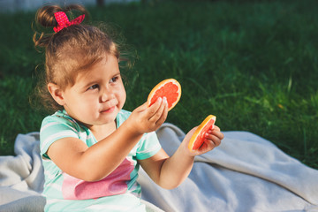 Small girl holds a slice of fresh grapefruit