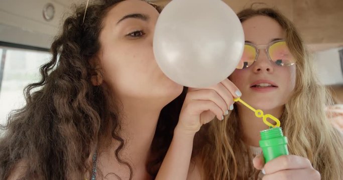 Portrait Beautiful Teenage hipster friends blowing soap bubbles having fun at festival in camper van on road trip adventure