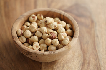 roasted hazelnuts in wood bowl on wooden table, copy space on the right side