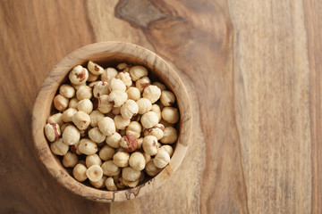 roasted hazelnuts in wood bowl on wooden table, copy space on the right side