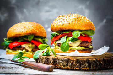 Tasty grilled beef burger with cheese, guacamole and pickled peppers. Dark background, brown paper, wooden stand.