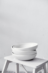 White empty ceramic plates stand in a pile stand on a wooden stool, kitchen equipment