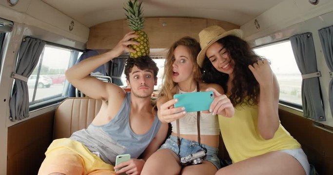 Beautiful best friends taking selfies photographing smart phone vintage camper van retro style social media smiling having fun acting with pineapple