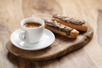 fresh espresso and eclairs with hazelnuts on wood table, sweet morning breakfast