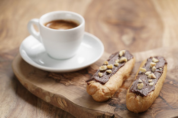fresh espresso and eclairs with hazelnuts on wood table, sweet morning breakfast
