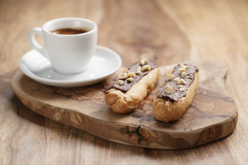 fresh espresso and eclairs with hazelnuts on wood table, sweet morning breakfast