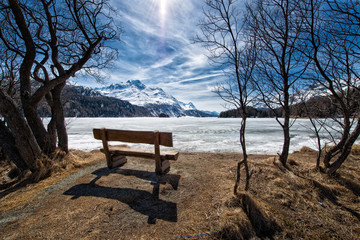 Fototapeta na wymiar Wooden bench to admire the scenery on an alpine lake ice