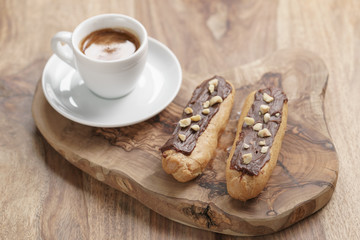 fresh espresso and eclairs with hazelnuts on wood table, sweet morning breakfast