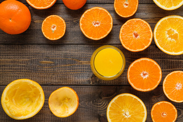 A glass of juice and cut oranges and mandarins on the wooden background