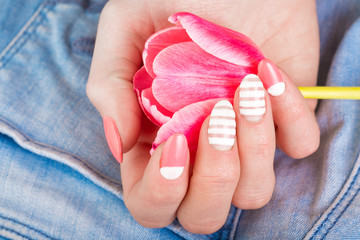 Obraz na płótnie Canvas A beautiful female manicure in pink, with a tulip flower against the background of blue jeans