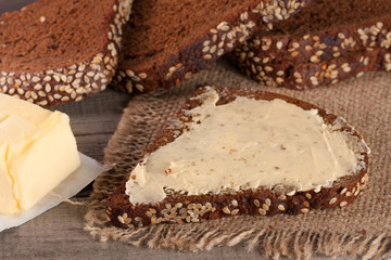 slices of black bread with sesame seeds and butter on an old wooden background