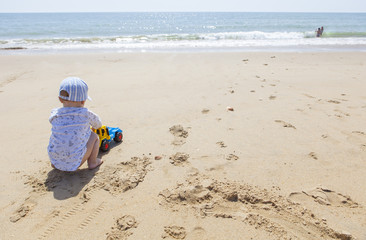 Fototapeta na wymiar Baby boy playing on the sand while other children splash beside beach shore