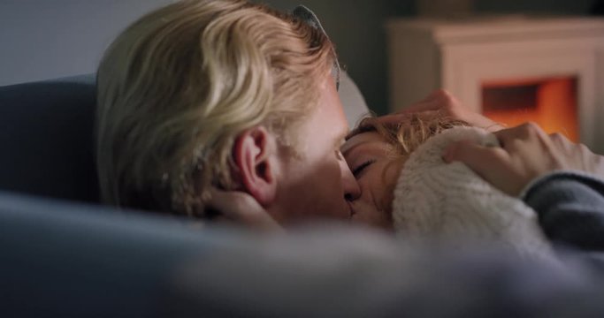 Attractive young couple sharing moment kissing at home on sofa by fireplace engaged in foreplay