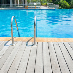 Swimming pool with stair and wooden deck at hotel.