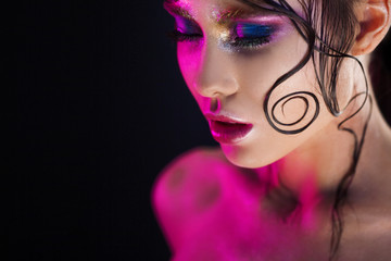 Young beautiful girl bright makeup with a wet look shine, dark background, pink light, disco style
