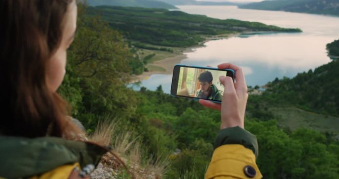 Young woman having video chat holding smartphone  webcam chatting to friend happy in nature at sunset