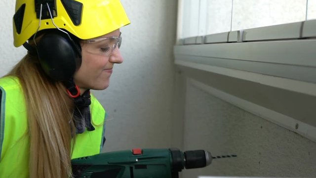 Young Female construction worker drilling concrete wall with the drill and smiling at the camera. Slow motion.