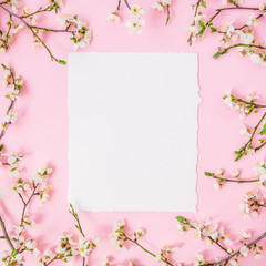 Frame of spring flowers and paper card on pink background. Flat lay, top view. Spring time background.