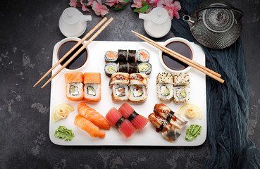 Japanese cuisine. Sushi set on a white plate over dark stone background.