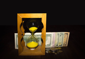 The glossy old-style hourglass standing with american dollar bills