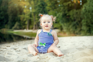 Cheerful baby girl sitting on the sand. The concept of childhood, leisure and lifestyle.